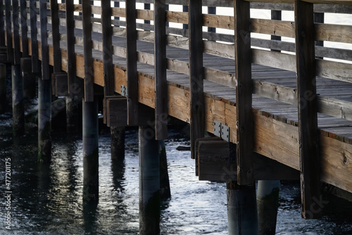 abstract diagonal view of a wooden footbridge over water with rows of wooden railings and rusty piers