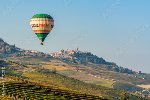 Hot air balloon flying over hills and vineyards during fall season surrounding La Morra village. In the Langhe region, Cuneo, Piedmont, Italy.