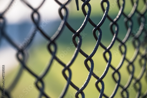 abstract closeup on a rusty chain link fence against a green and blue background with selective focus on one link surrounded by a repeating pattern of blurred links at a slight diagonal