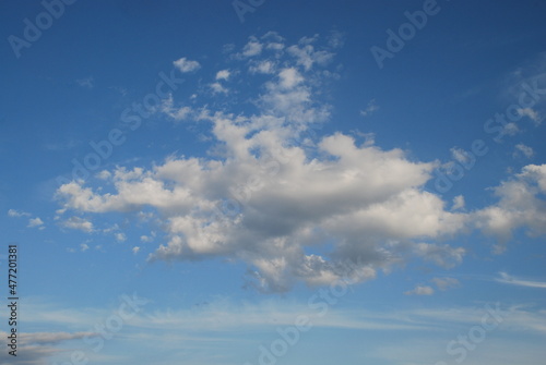 A whimsical white cloud. A small cumulus cloud floats in the light blue sky. It has an interesting shape, from above the cloud is white from below, light gray.