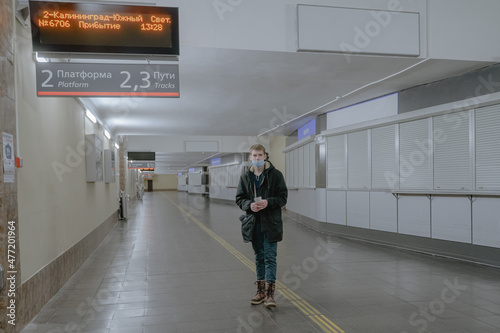 a young man in a medical mask, in a public corridor, heading for a train station