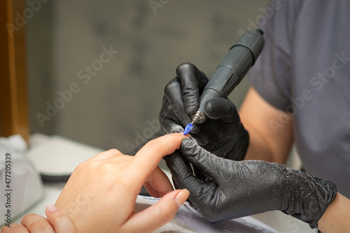 Manicurist removes nail polish uses the electric machine of the nail file during manicure in a nail salon photo