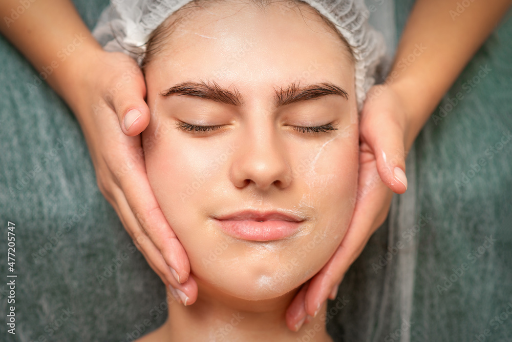 Naklejka premium Spa facial skincare. Close-up of a young caucasian woman getting spa moisturizing face massage treatment at beauty spa salon