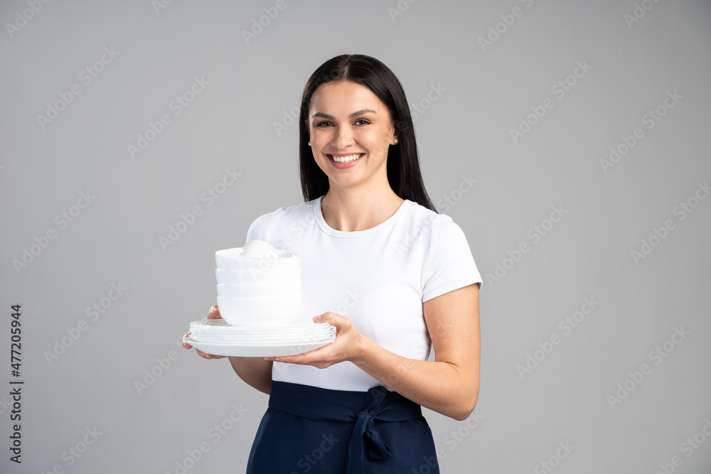 Waist up portrait view of the attractive woman waitress holding a lot of empty plates and smiling to the camera isolated on grey background. Stock photo Waist up portrait view of the attractive woman waitress holding a lot of empty plates and smiling to the camera isolated on grey background. Stock photo