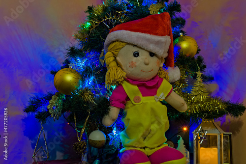 Lalka szmaciana w czapce Świętego Mikołaja . Choinka , bombki , lampki . Boże Narodzenie .
