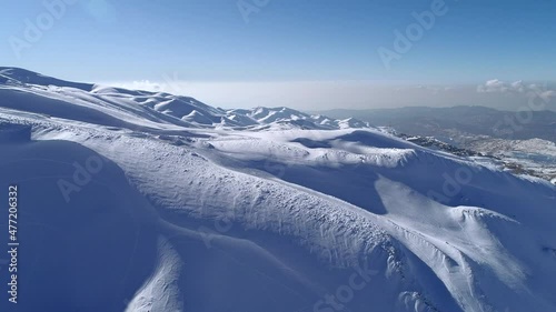 Aerial winter view with mountains covered by snow. Mountain peak with fresh snow. Flying over the ski slopes.