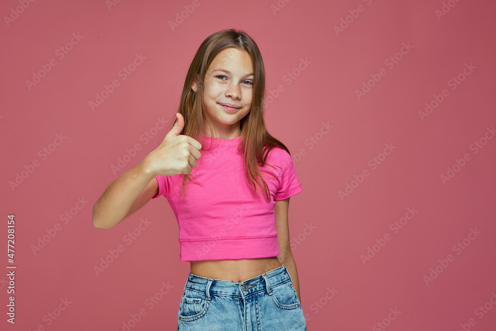 Positive child girl showing thumb up gesture, like sign, smiling recommend good or service on pink studio background Positive child girl showing thumb up gesture, like sign, smiling recommend good or service on pink studio background
