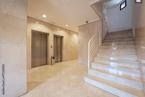 Entrance portal to a building with cream marble floors and walls  stairs and metal elevators
