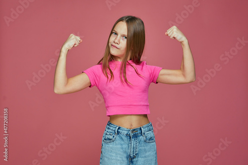 Powerful sporty child girl show biceps muscles, raising hands on pink studio background. Girls rules concept