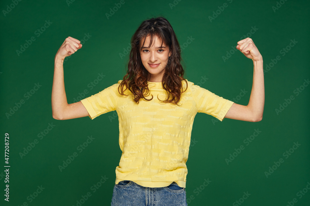 Pretty young girl show hands muscles, power, feel proud about achievements, keeps fit and healthy on green background
