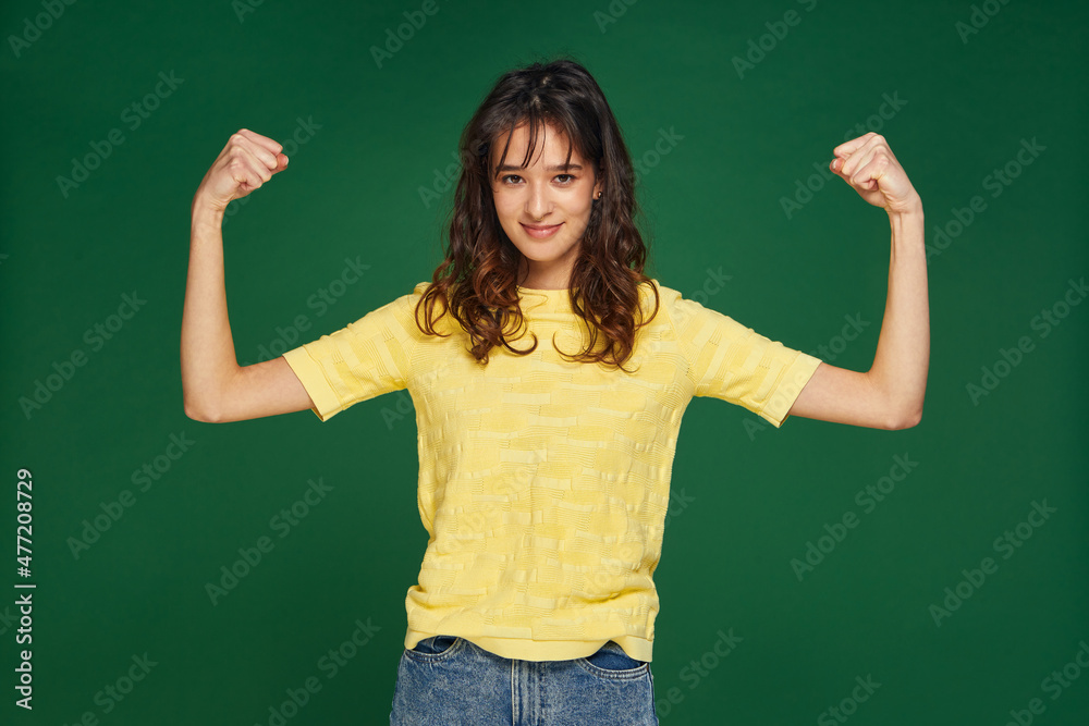 Pretty young girl show hands muscles, power, feel proud about achievements, keeps fit and healthy on green background Pretty young girl show hands muscles, power, feel proud about achievements, keeps fit and healthy on green background