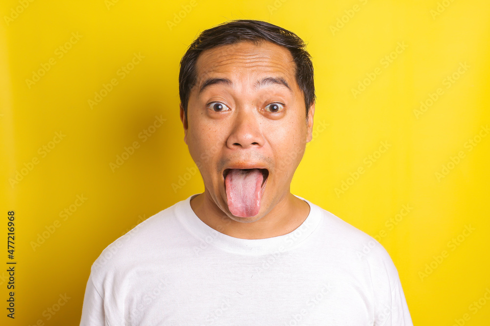 Close-up portrait of asian man with reproachful expression, mocking, sticking out tongue isolated on yellow background Close-up portrait of asian man with reproachful expression, mocking, sticking out tongue isolated on yellow background