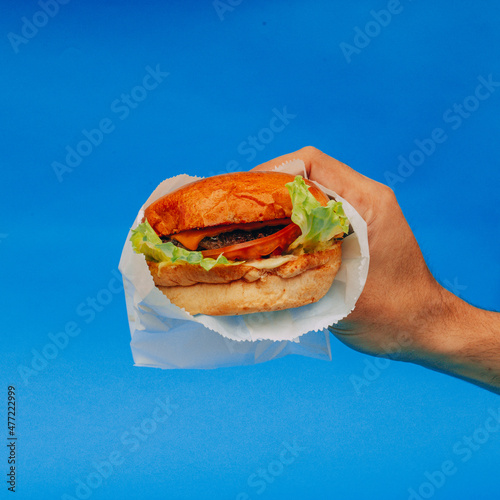 Hamburguesa deliciosa comida rápida sostenida con la mano de un hombre con fondo azul