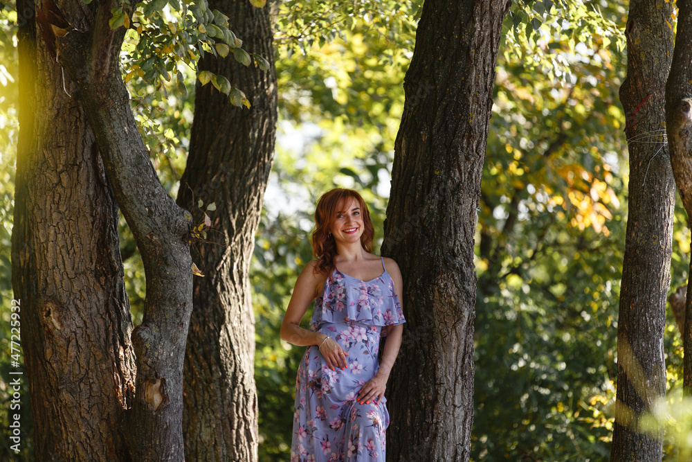 Young dreaming happy smiling woman in a park among the old trees. Young woman weared in romantic dress walking among beautiful nature. Me time. Summer story. Brown-haired girl with long hairs. Young dreaming happy smiling woman in a park among the old trees. Young woman weared in romantic dress walking among beautiful nature. Me time. Summer story. Brown-haired girl with long hairs.