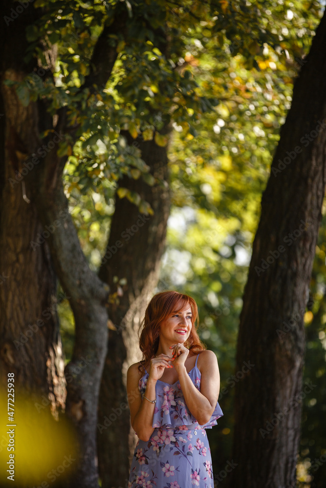 Young dreaming happy smiling woman in a park among the old trees. Young woman weared in romantic dress walking among beautiful nature. Me time. Summer story. Brown-haired girl with long hairs. Young dreaming happy smiling woman in a park among the old trees. Young woman weared in romantic dress walking among beautiful nature. Me time. Summer story. Brown-haired girl with long hairs.