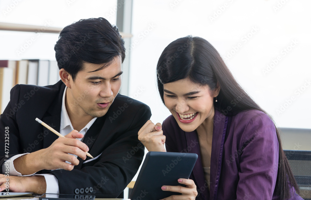 Millennial Asian happy professional successful male businessman and female businesswoman colleague in formal outfit sitting at working desk take break holding tablet have fun conversation together
