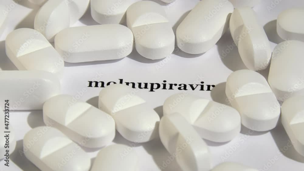 The first covid antiviral drug for oral administration concept. Shadows. Molnupiravir. Closeup shot of white tablets on white background. Black text. Camera slowly rotating. The first covid antiviral drug for oral administration concept. Shadows. Molnupiravir. Closeup shot of white tablets on white background. Black text. Camera slowly rotating.