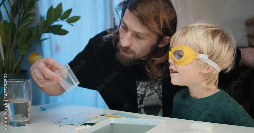 Family together young man with children boy reading manual for making chemical experiment at home. Preschool kid learning with father to prepare crystals. Carefree childhood and home education