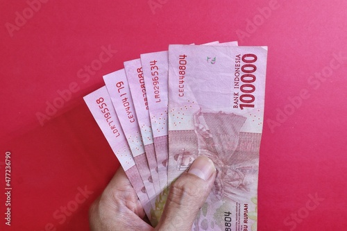 Rupiah the official currency of Indonesia. Business and finance concept. Uang 100000 Rupiah. Bank Indonesia. Red Background, Negative space, Copy space.