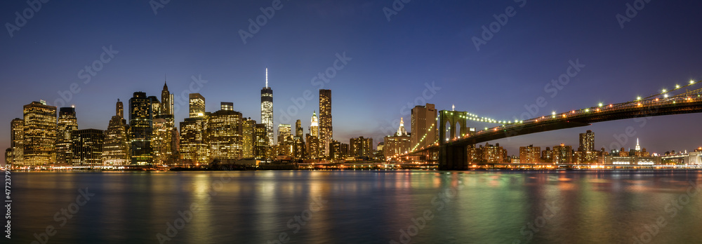 Panoramic view of Manhattan with the Brooklyn Bridge at night.