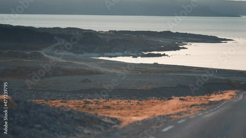 Driving along the rugged rocky coastline of Varanger peninsula. The setting sun is lighting the parches of the orange grass. photo