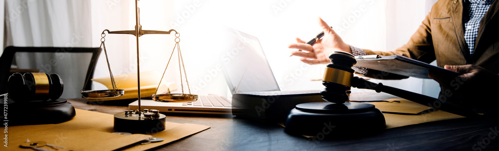 Justice and Law concept. Legal counsel presents to the client a signed contract with gavel and legal law or legal having team meeting at law firm in background Justice and Law concept. Legal counsel presents to the client a signed contract with gavel and legal law or legal having team meeting at law firm in background