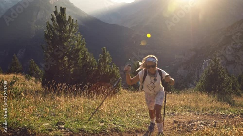 Blonde woman hiking uphill with trekking poles, Benasque, Spain, medium shot photo