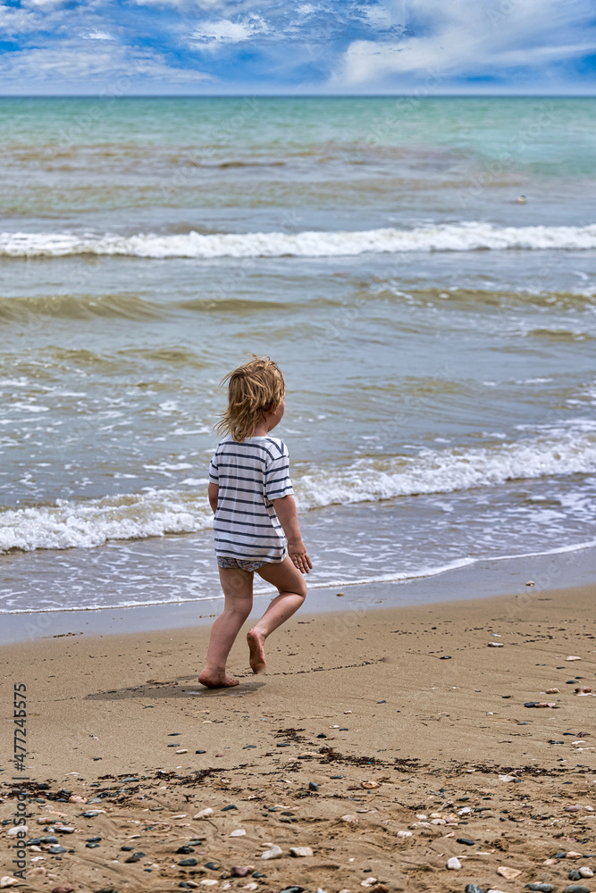 A little boy runs along the sandy beach along the seashore