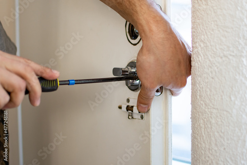 Closeup of a locksmith installing or repairing a new deadbolt lock on a house exterior door. Man fixing lock with screwdriver.