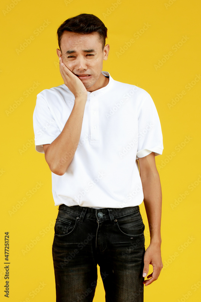 Poor young Asian man in shirt and jeans frowning and put hand on cheek as getting sick and sufferring from pain and hurt of toothache because of oral disease Poor young Asian man in shirt and jeans frowning and put hand on cheek as getting sick and sufferring from pain and hurt of toothache because of oral disease