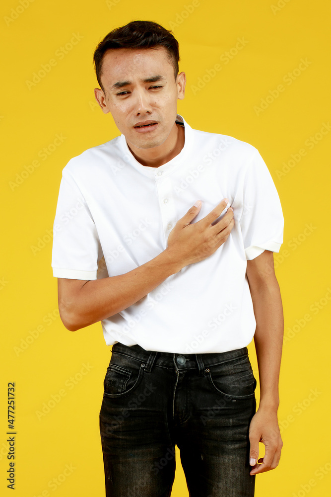 Sick young Asian guy in casual shirt and jeans catch his chest and frowning as feeling unwell of heart muscle failure Sick young Asian guy in casual shirt and jeans catch his chest and frowning as feeling unwell of heart muscle failure