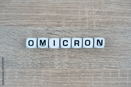 A white cube written Omicron over wooden table. New Variant. Coronavirus Mutation