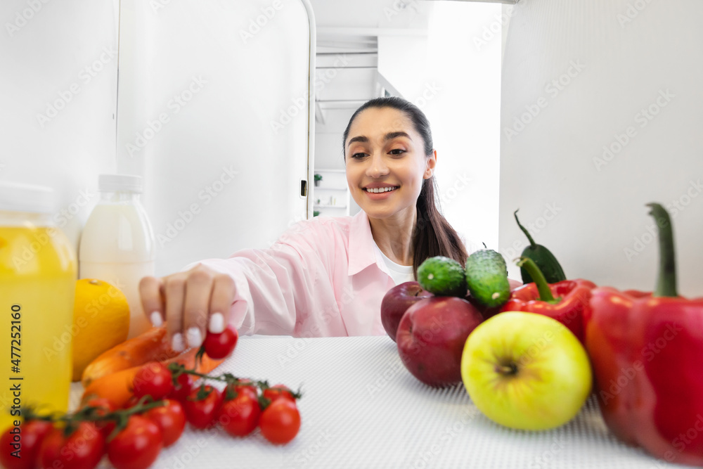 Smiling woman opening fridge and taking food