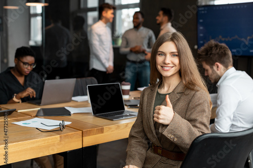 Confident businesswoman sitting at desk showing thumbs up gesture