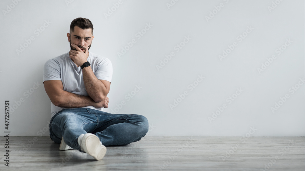 Young depressed man sit against gray wall at home feeling unhappy, lonely and sad in depression