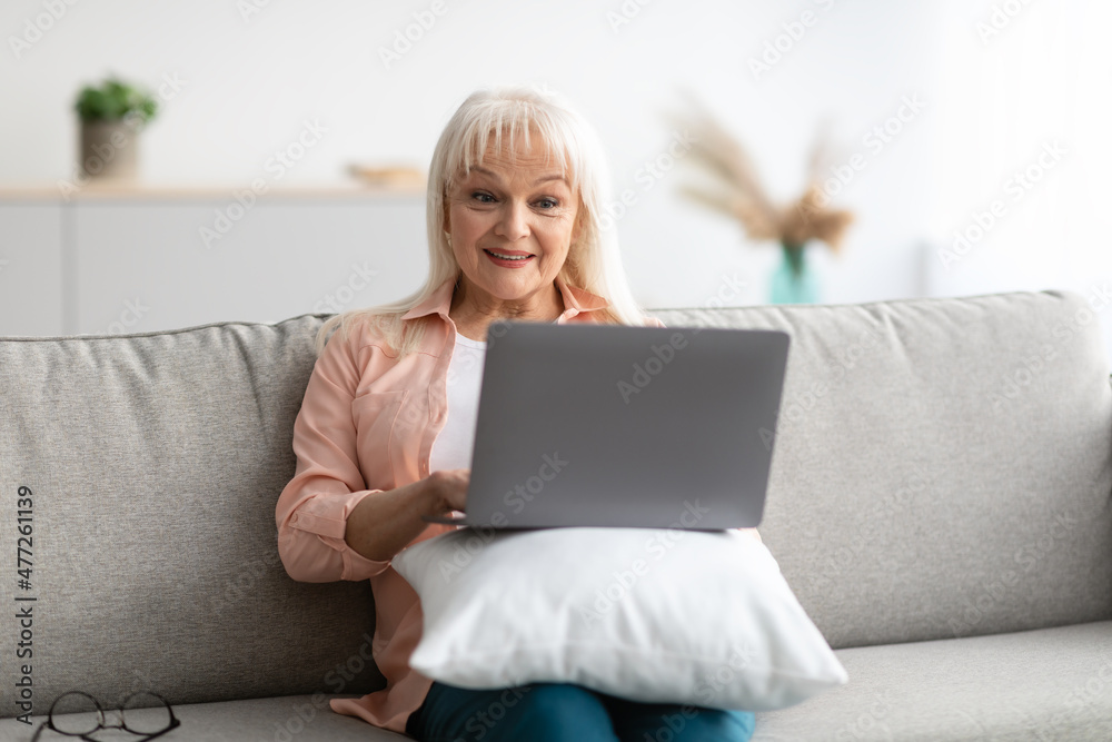Happy mature woman sitting on couch and using computer Happy mature woman sitting on couch and using computer