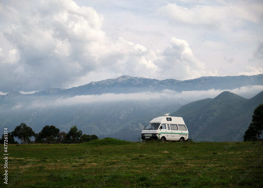 Caravana frente a un paisaje montañoso en el que vemos cumbres y nubes