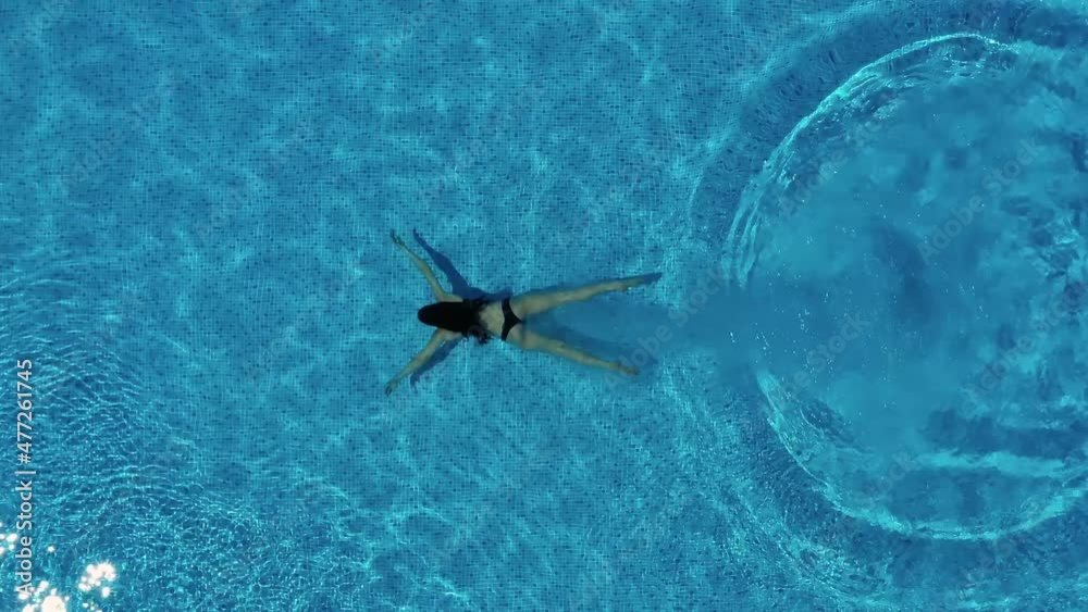 Girl is diving into the swimming pool and splashing water. Drone aerial view. Summer vacation concept