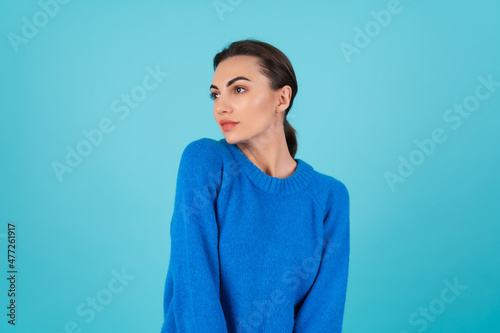Young woman in blue knitted sweater and natural day makeup on turquoise background
