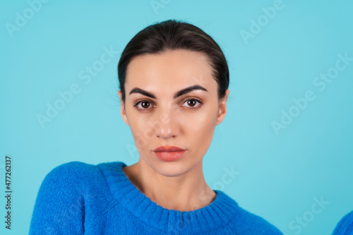 Beauty portrait of a young woman in a blue knitted sweater and natural day makeup  full lips with nude matte lipstick and perfect eyebrows  looks at the camera