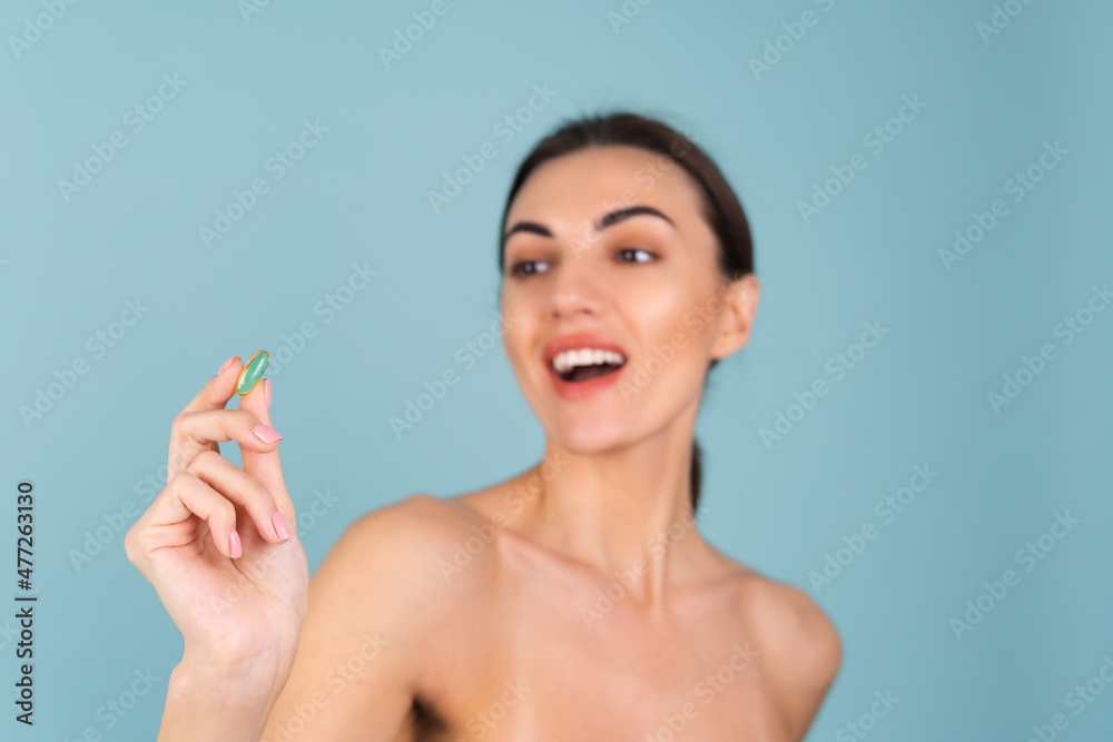 Close-up beauty portrait of a topless woman with perfect skin and natural make-up, holding a supplement, vitamin omega 3, fish oil, on a turquoise background Close-up beauty portrait of a topless woman with perfect skin and natural make-up, holding a supplement, vitamin omega 3, fish oil, on a turquoise background