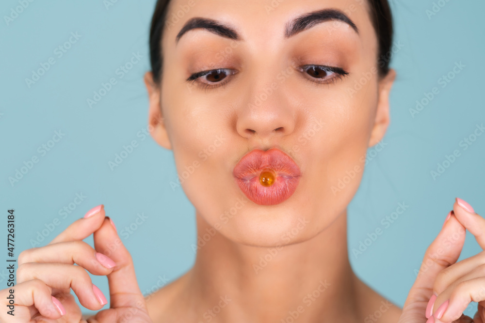 Close-up beauty portrait of a topless woman with perfect skin and natural make-up, holding a supplement, vitamin omega 3, fish oil, on a turquoise background Close-up beauty portrait of a topless woman with perfect skin and natural make-up, holding a supplement, vitamin omega 3, fish oil, on a turquoise background
