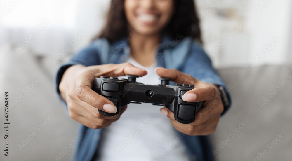 Free time. Happy african american woman holding gamepad playing online video game in living room, selective focus