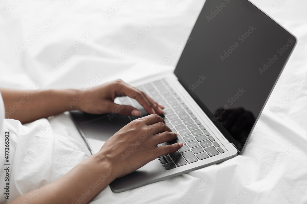 African american female hands typing on laptop computer with empty screen, sitting in bed, closeup, free space, mockup African american female hands typing on laptop computer with empty screen, sitting in bed, closeup, free space, mockup