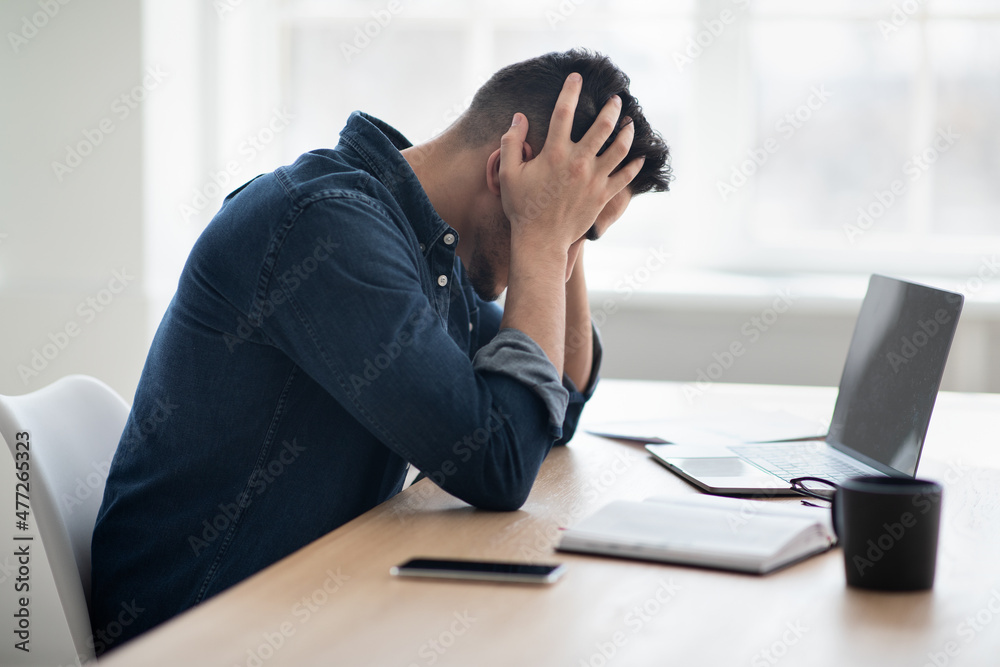 Exhausted arab man sitting in front of laptop, office interior Exhausted arab man sitting in front of laptop, office interior