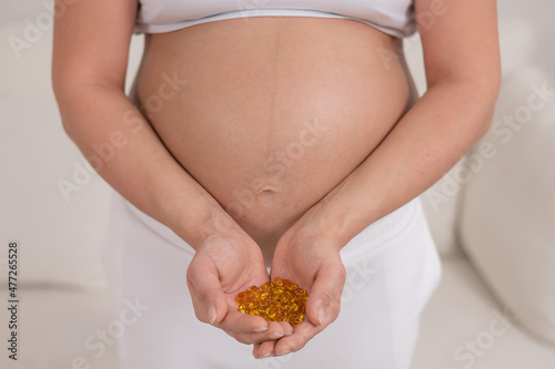 A pregnant woman with a bare belly holds a handful of vitamins. Transparent golden pills. Vitamin D for the expectant mother.
