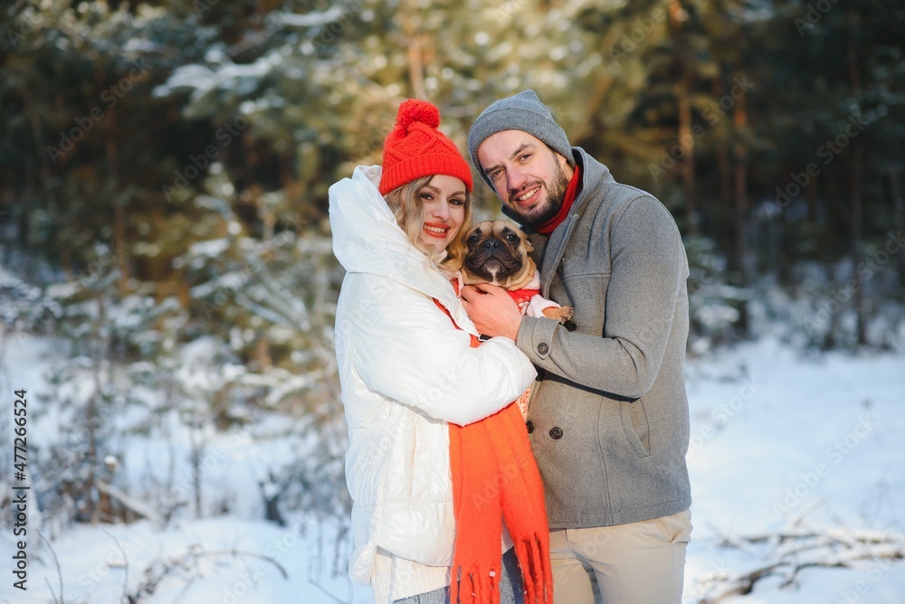 Young couple in love with dog walking in the snowy forest.
