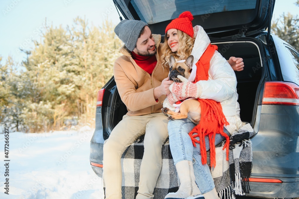 lovely smiling couple sitting in car trunk in winter forest
