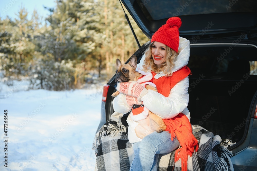 Young woman with dog sitting in open trunk of car. winter forest vacation.