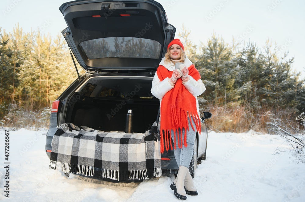 With cup of drink. Beautiful young woman is outdoors near her automobile at winter time.